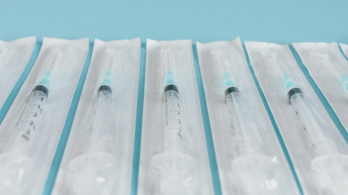 Array of sterile syringes in individual packaging against a blue background.