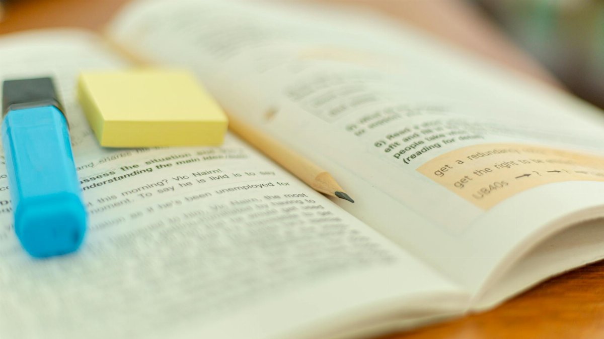Close-up of an open book with a highlighter and sticky notes for study reference.