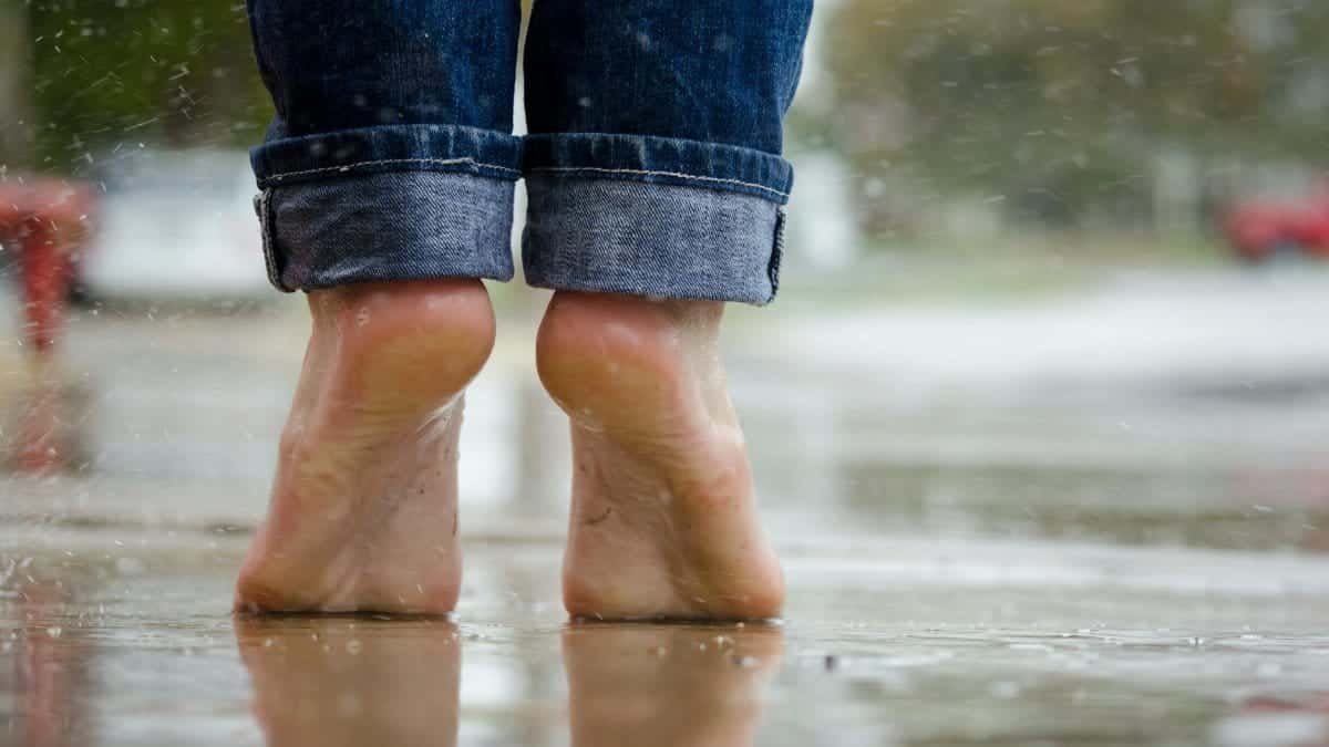 Close-up of bare feet on a wet pavement, capturing calm and connection with nature.