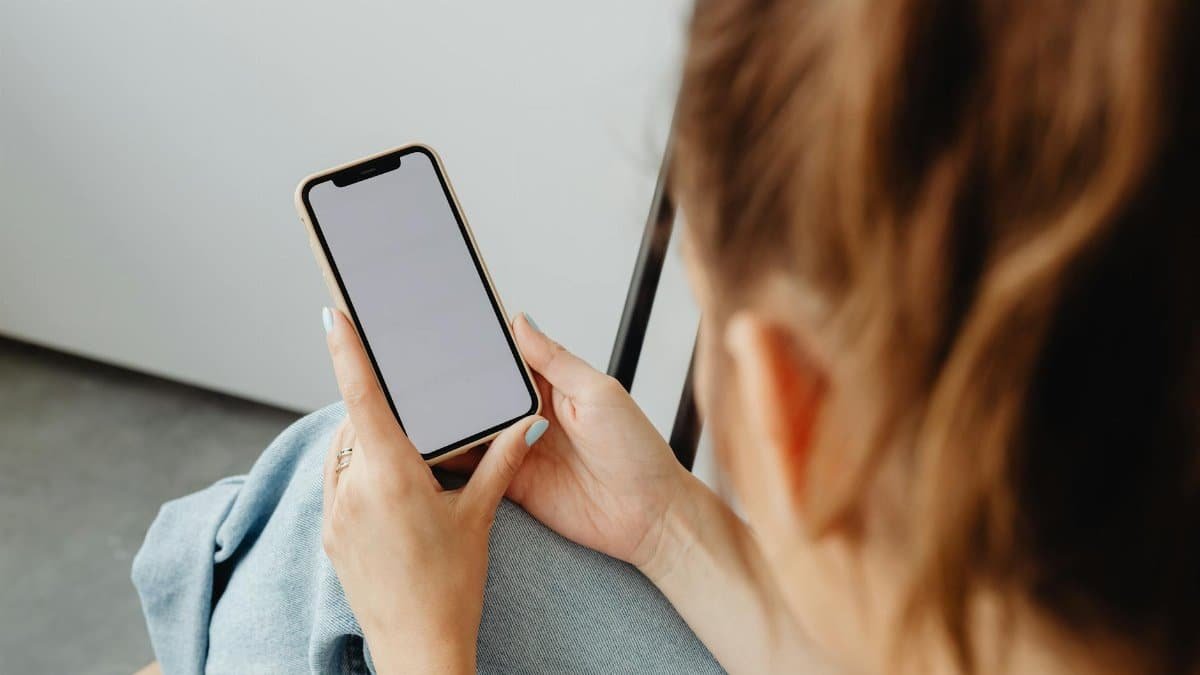 A woman holds a smartphone with a blank screen indoors, offering a mockup opportunity.
