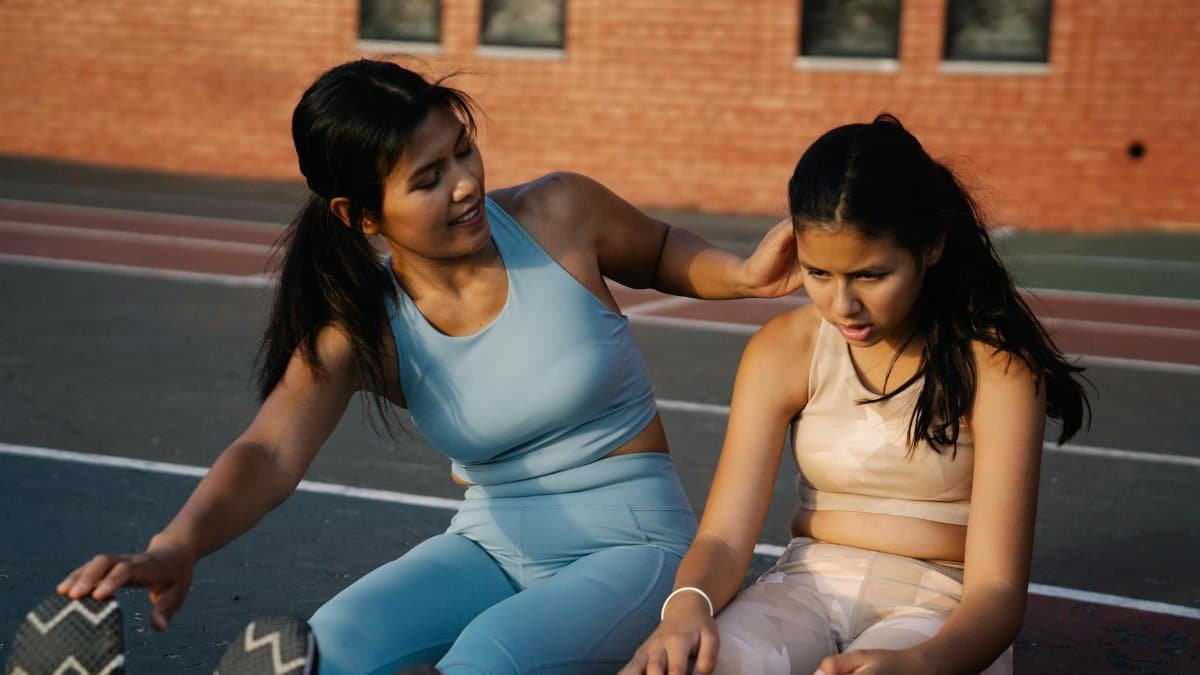 Mother and daughter engaged in stretching exercises on an outdoor sports track.