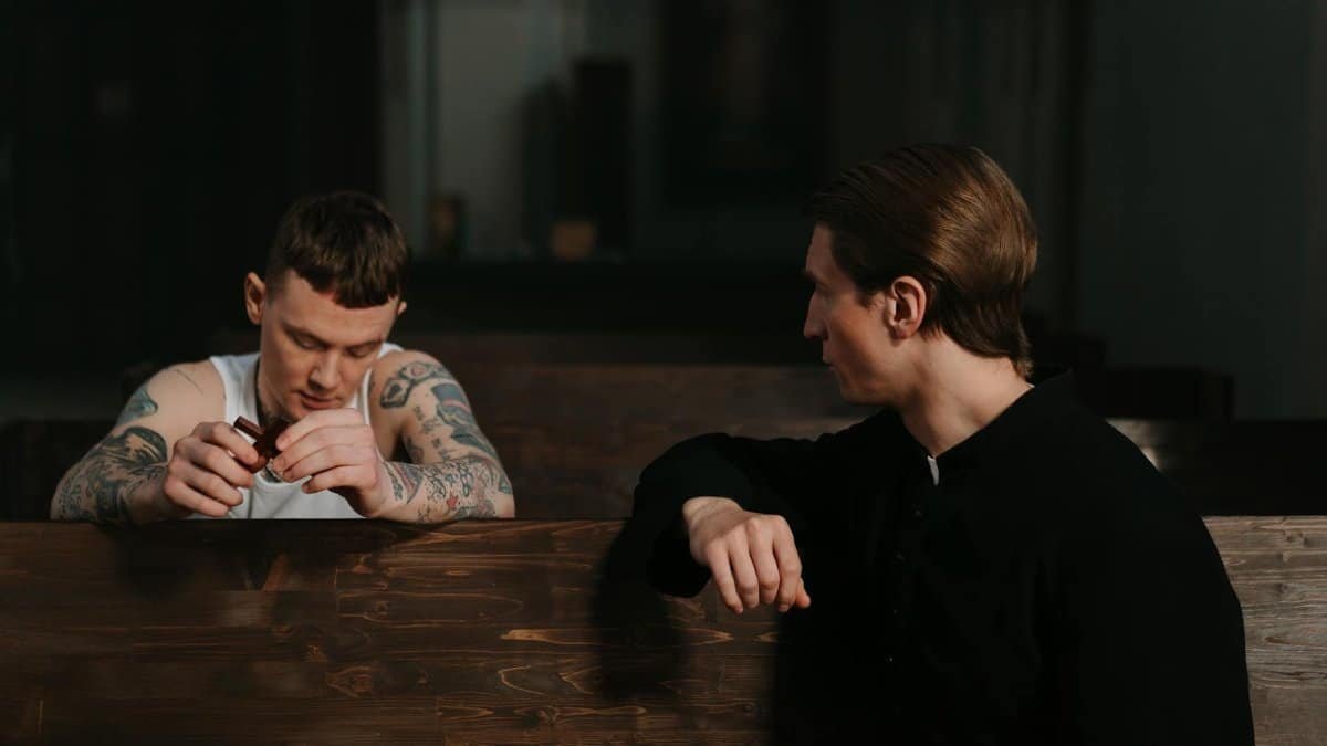 A tattooed man in conversation with a priest inside a church, sharing a moment of confession.