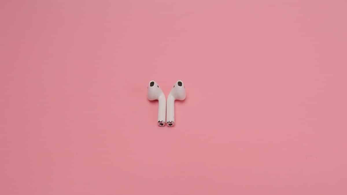 Modern wireless earbuds on a pastel pink background, showcasing minimal tech design.