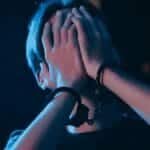 A person in handcuffs conceals their face under a blue light, suggesting a crime scene.