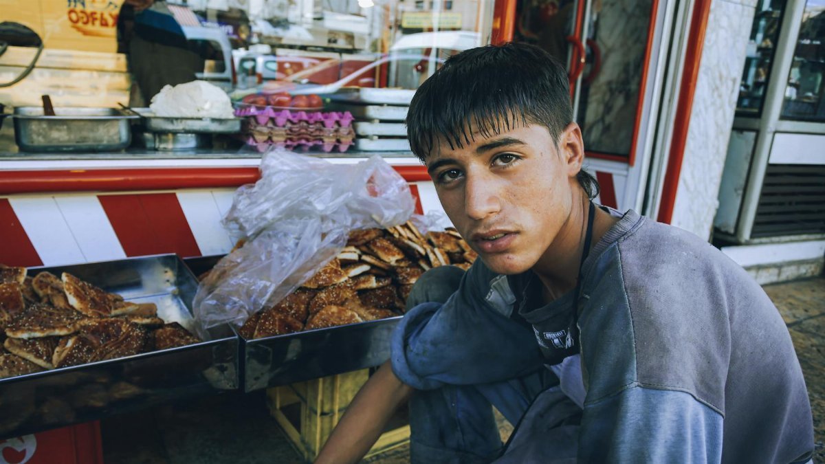 Teenage boy in casual clothing sitting beside a street pastry stall, showcasing urban commerce.