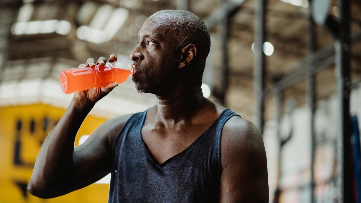 A fit adult man drinks a cold beverage while taking a break from his workout at the gym.
