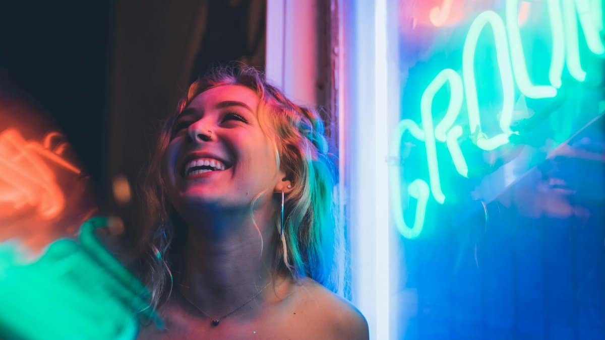 Smiling woman enjoying nightlife with vibrant neon signs, capturing a lively mood.