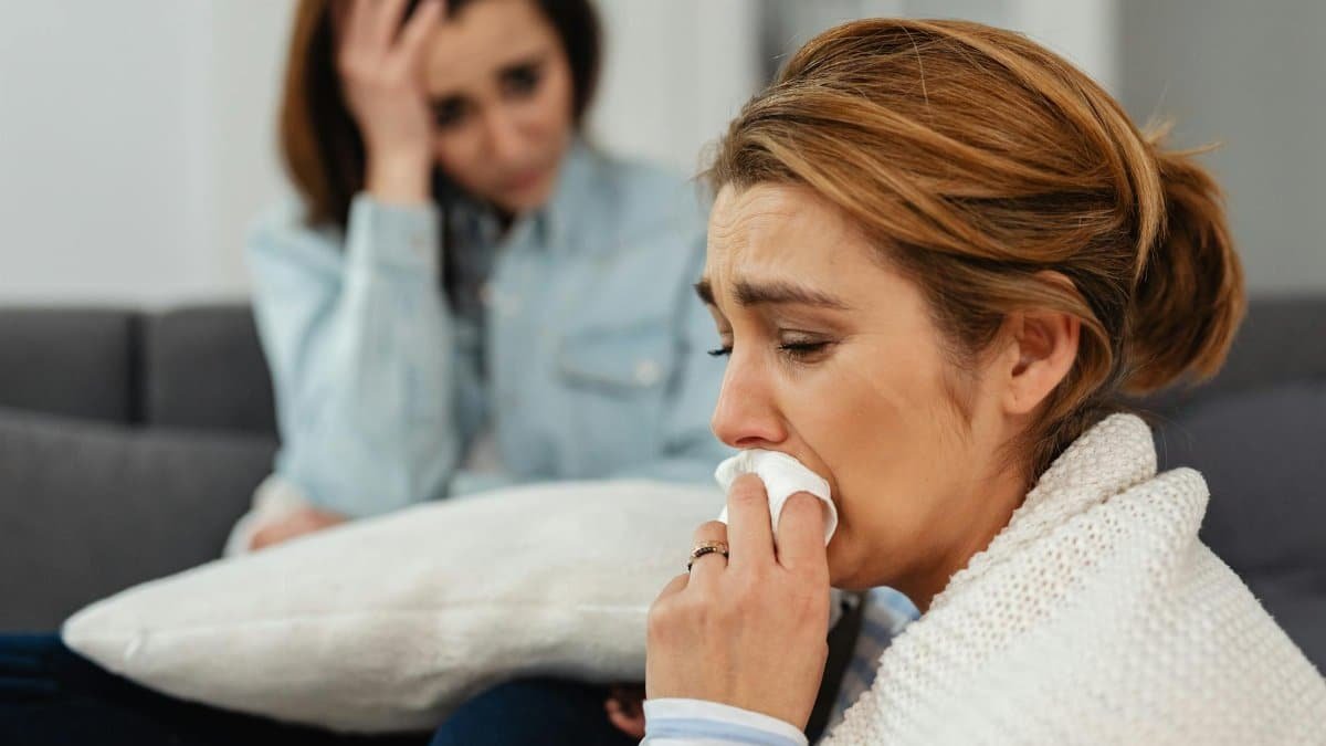Two women sitting on a couch, expressing and sharing emotions of sadness and support.