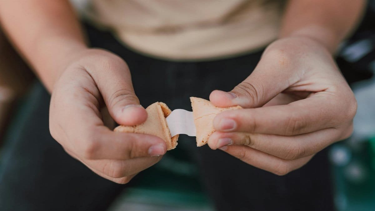 Hands breaking open a fortune cookie with a blank paper slip emerging.
