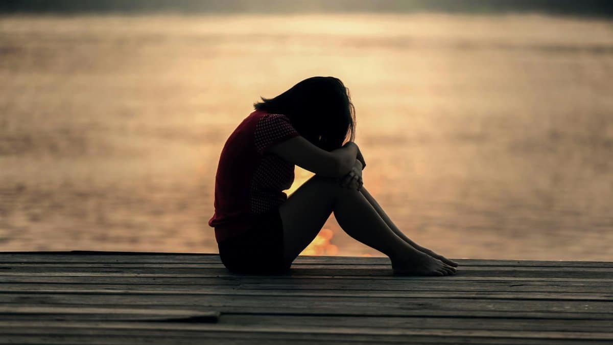 A woman sitting alone on a wooden dock by the lake, showing solitude and reflection.