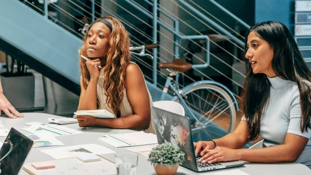Diverse women engaging in a collaborative meeting at an office desk, focused on planning and innovation.