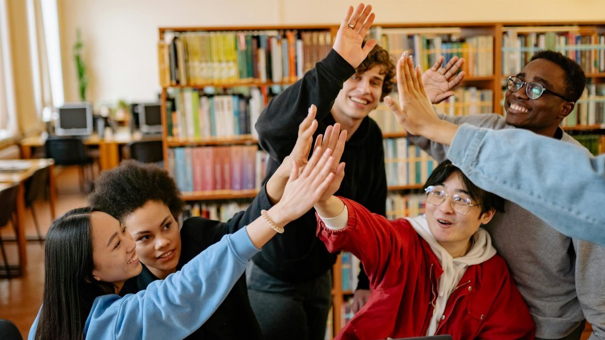 Group of happy students high-fiving in a library setting, celebrating success.