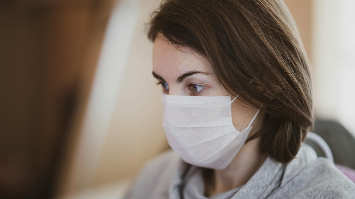 Close-up side view of a woman wearing a face mask indoors, embodying new normal health precautions.