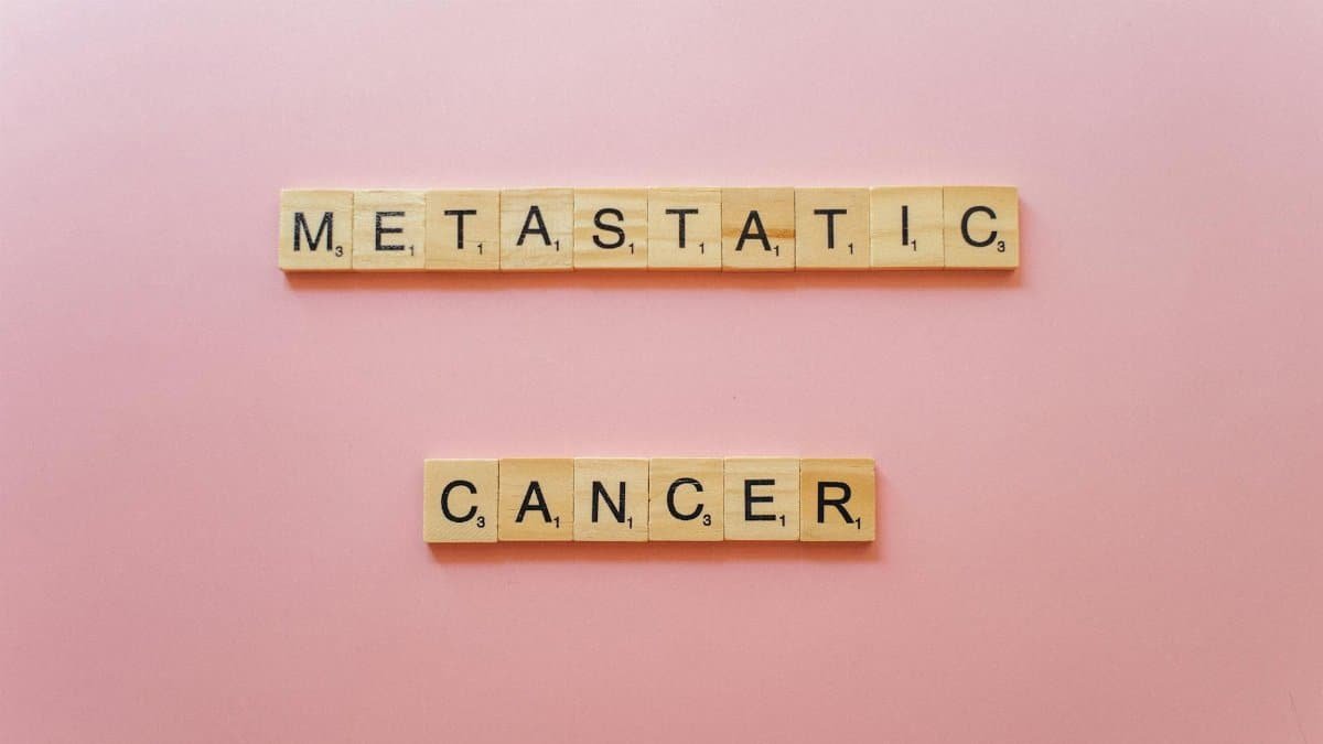Scrabble tiles spell 'Metastatic Cancer' on pink background, symbolizing awareness.