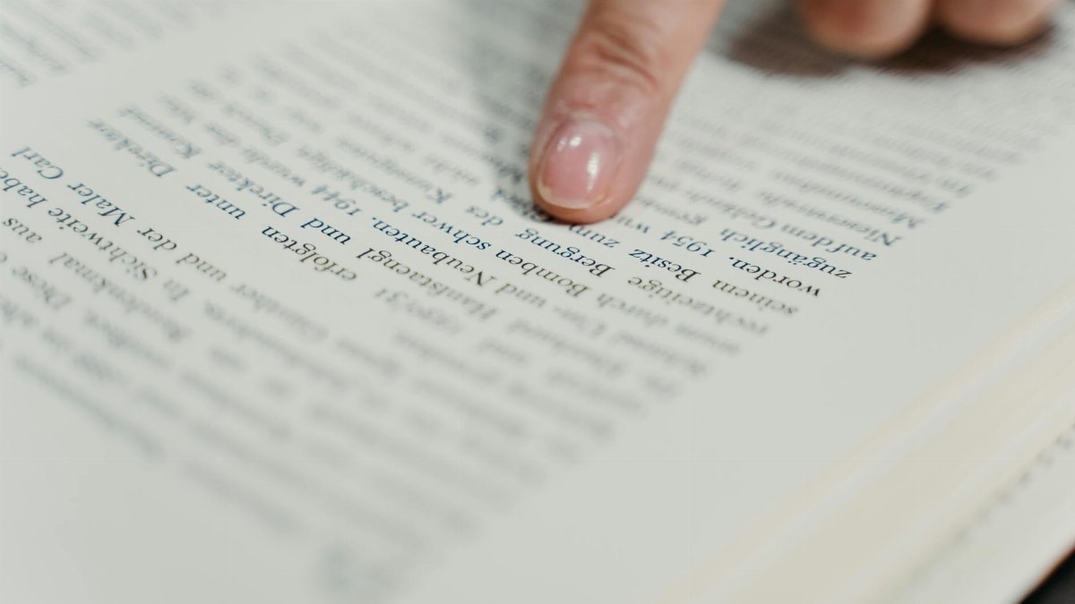 A detailed view of a finger pointing at text in a book, emphasizing reading and study.