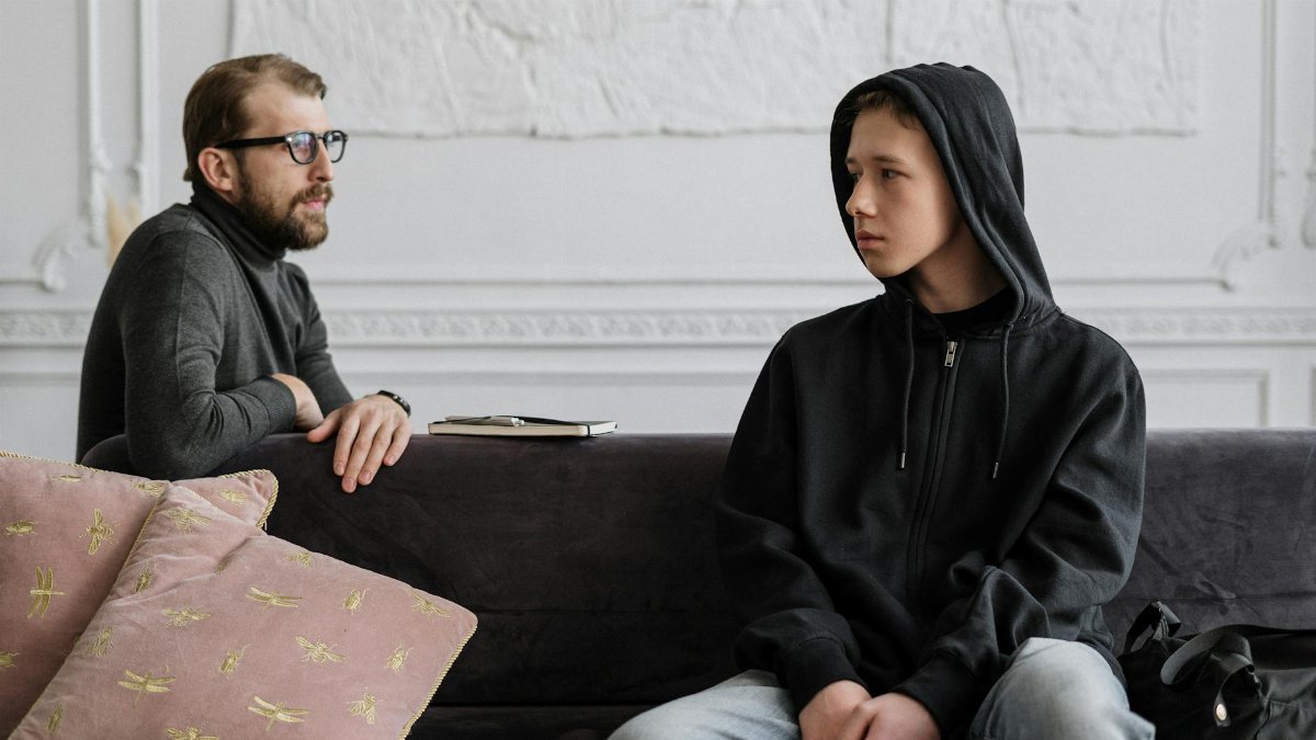 A therapist and a teenage boy discuss mental health issues in a modern office setting.
