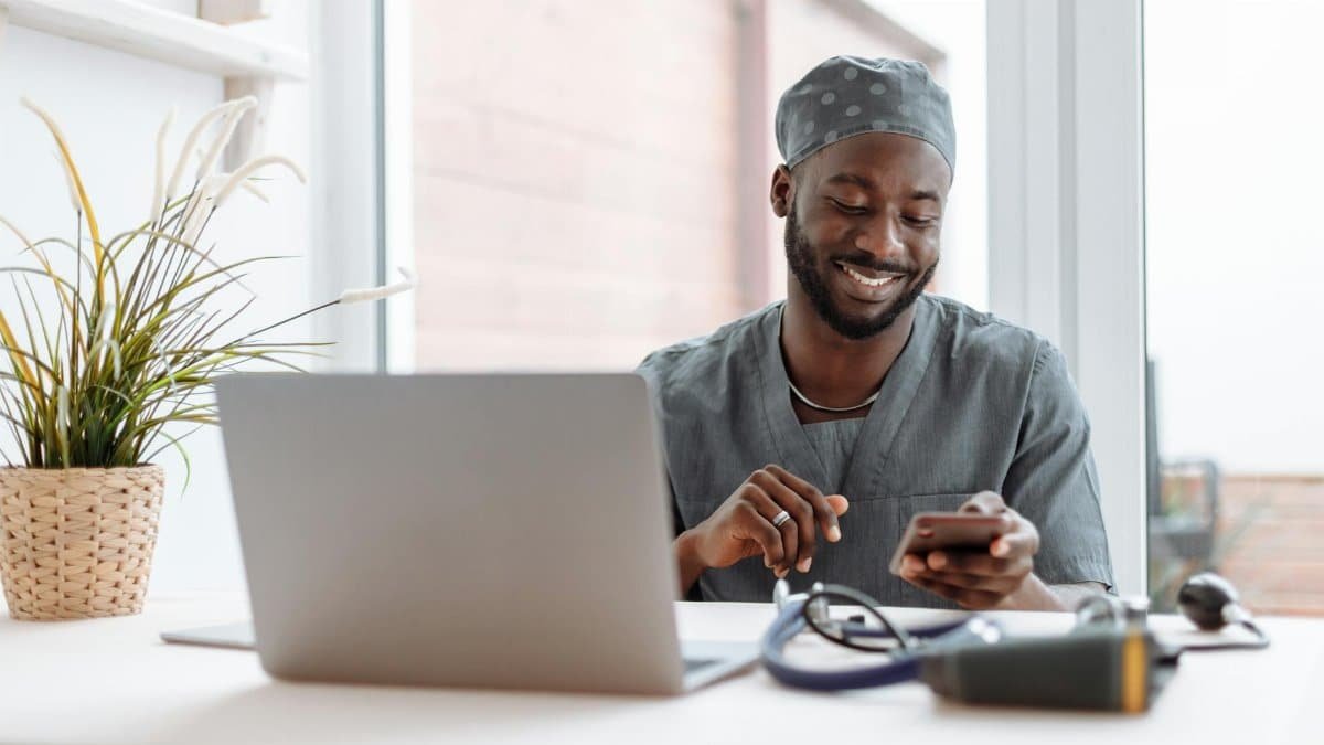 Smiling healthcare professional using phone in office with laptop and medical tools.