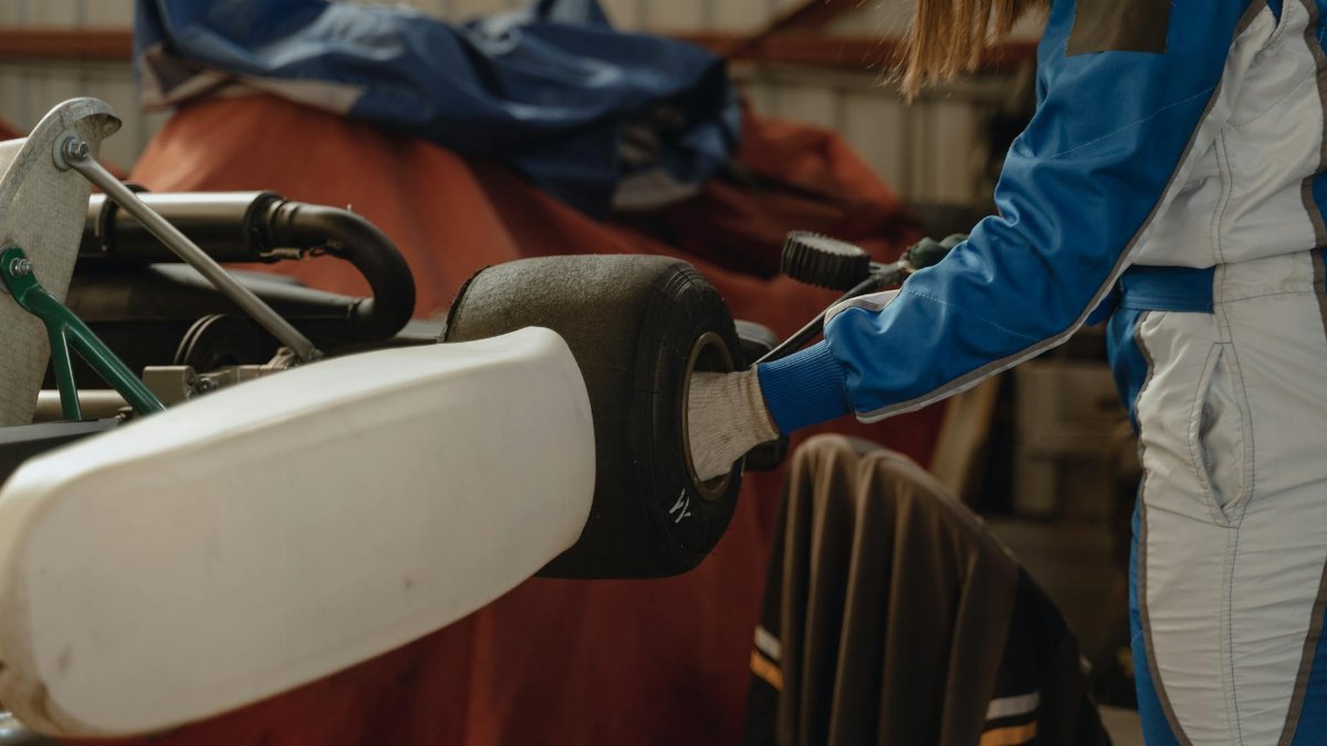 A young driver in a racing suit adjusts their go-kart indoors, preparing for a competition.