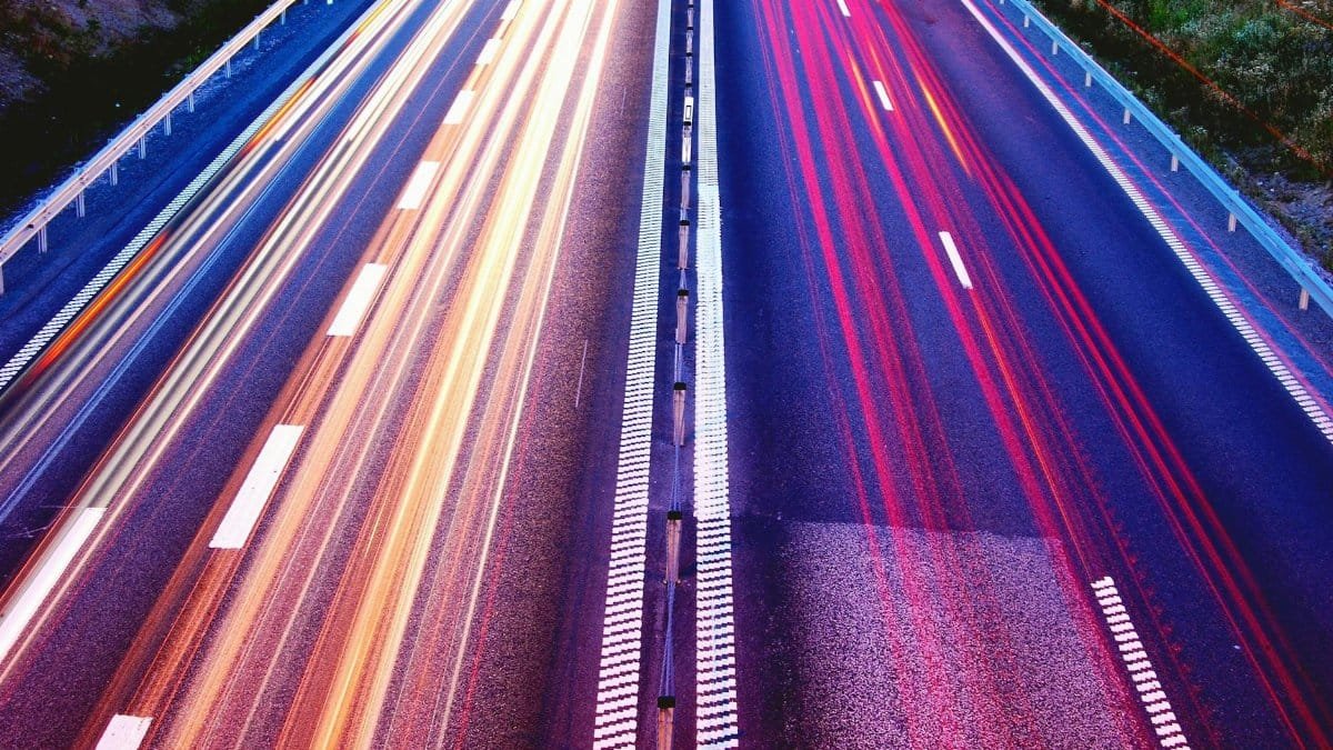 Long exposure capture of vibrant light trails on a highway at dusk, showcasing motion and speed.