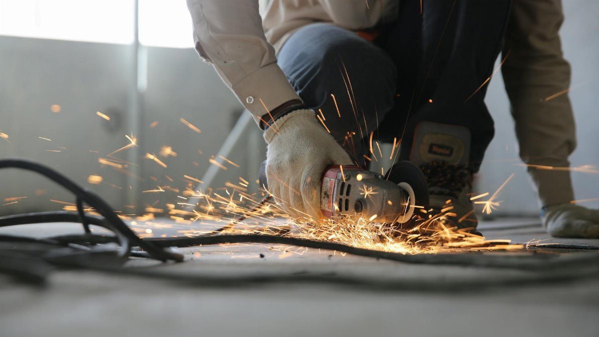A skilled industrial worker uses a grinder creating a burst of sparks indoors.