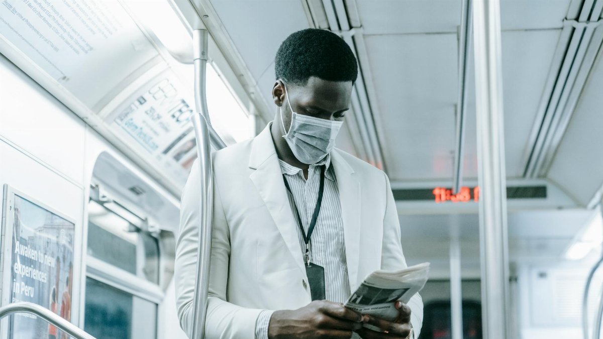 A man in a face mask reads a newspaper on public transportation during the pandemic.