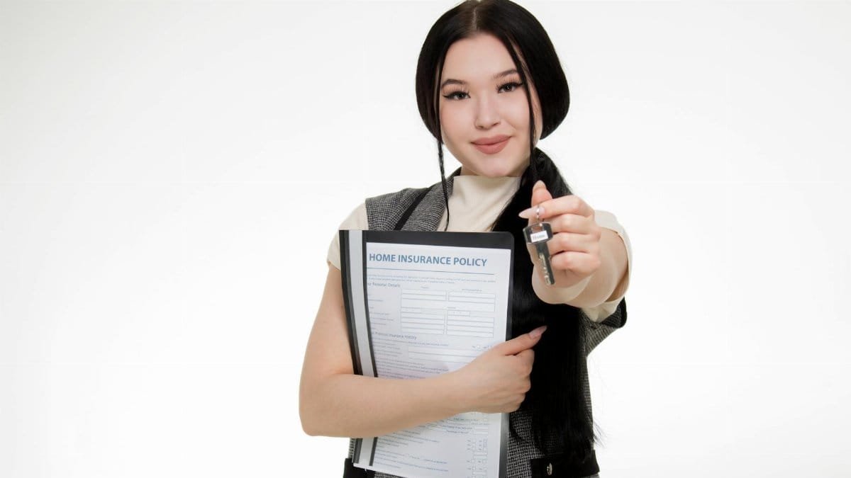 Asian woman smiling while holding a home insurance policy and a key, symbolizing new home ownership.