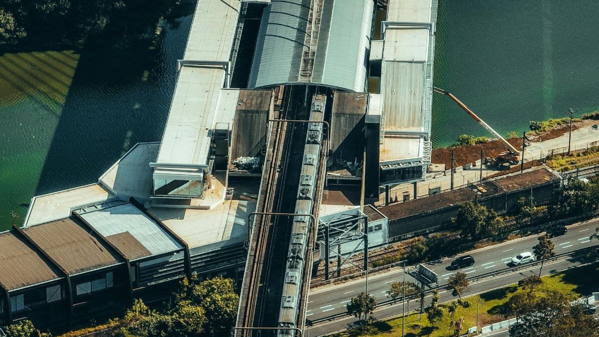 Aerial perspective of a train station by a river, highlighting urban transportation.