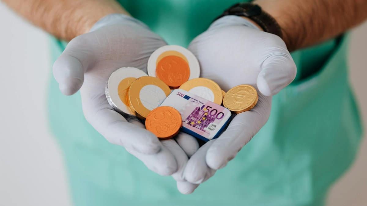 A healthcare worker with gloves holding Euro coins and a bill, symbolizing medical finance.