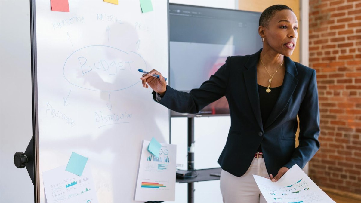 Professional businesswoman explaining budget strategy on a whiteboard during a meeting.