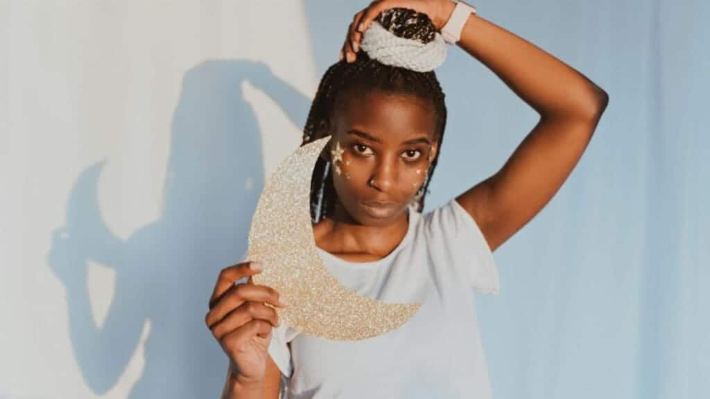 Artistic portrait of a woman holding a glittery crescent moon, adorned with star face art.