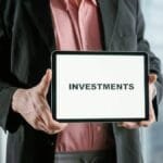 Professional holding a tablet with 'INVESTMENTS' text, ideal for finance and business themes.