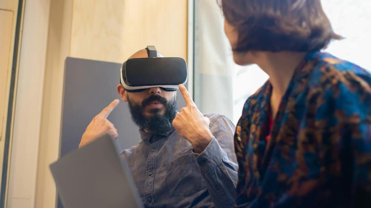 A man and woman explore virtual reality technology indoors with a laptop and VR goggles.