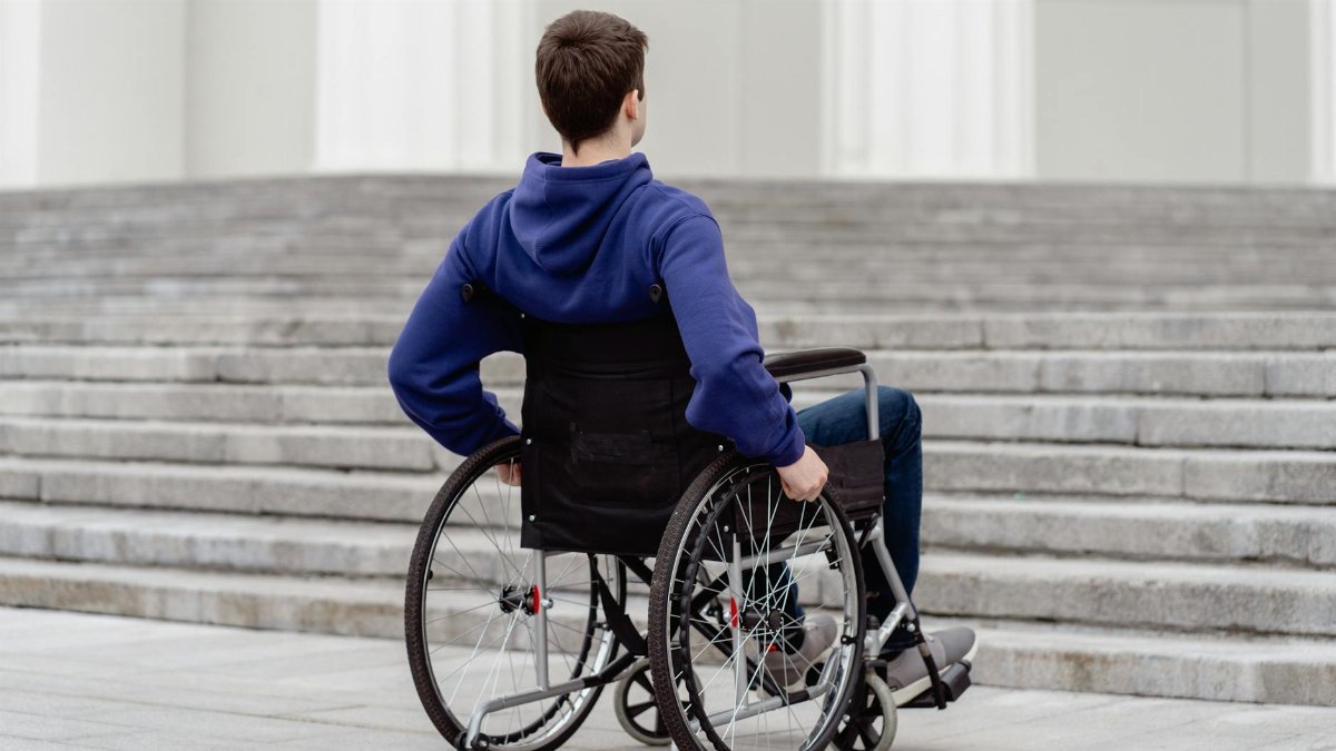 Back view of a young man in a wheelchair facing steps in a city setting.