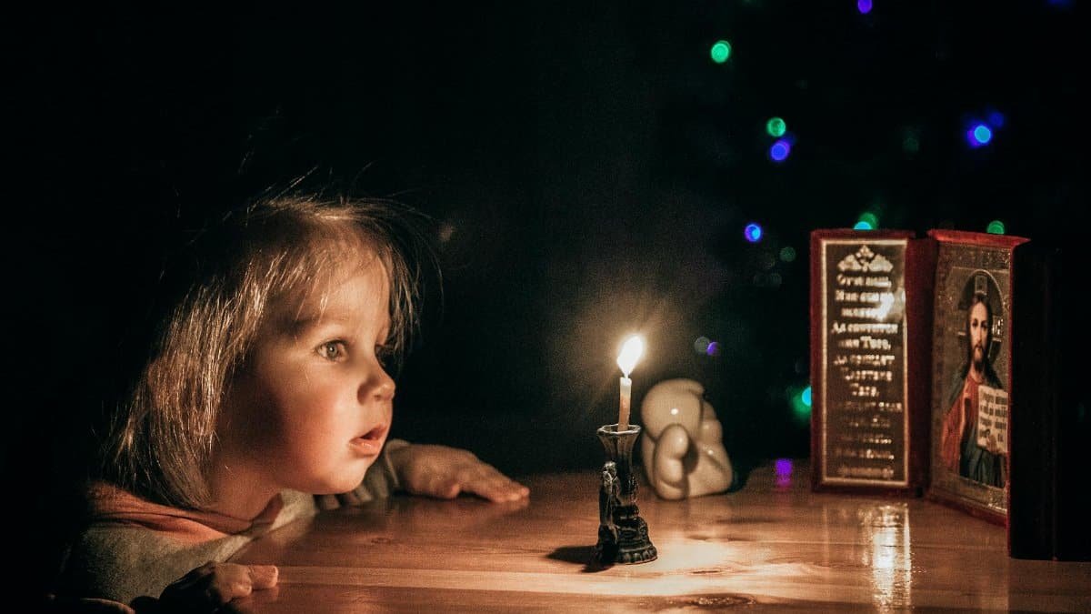 A young girl gazes in awe at a candlelight, surrounded by a serene, dark ambiance.