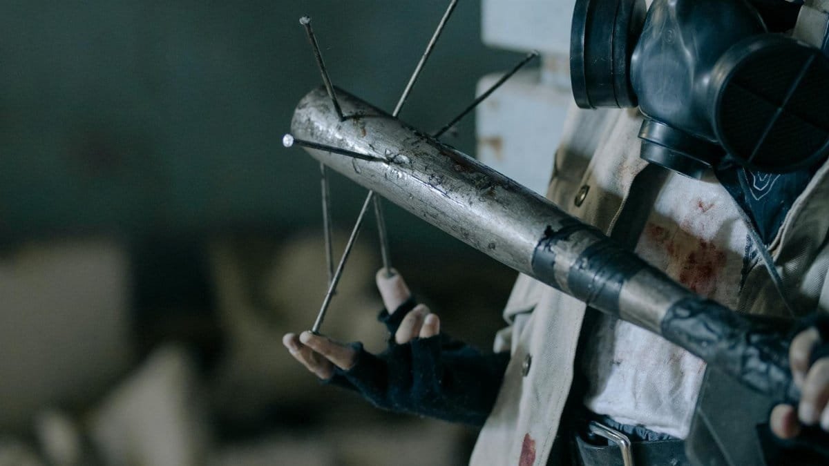 Close-up of a person with a gas mask holding a makeshift melee weapon in a post-apocalyptic setting.