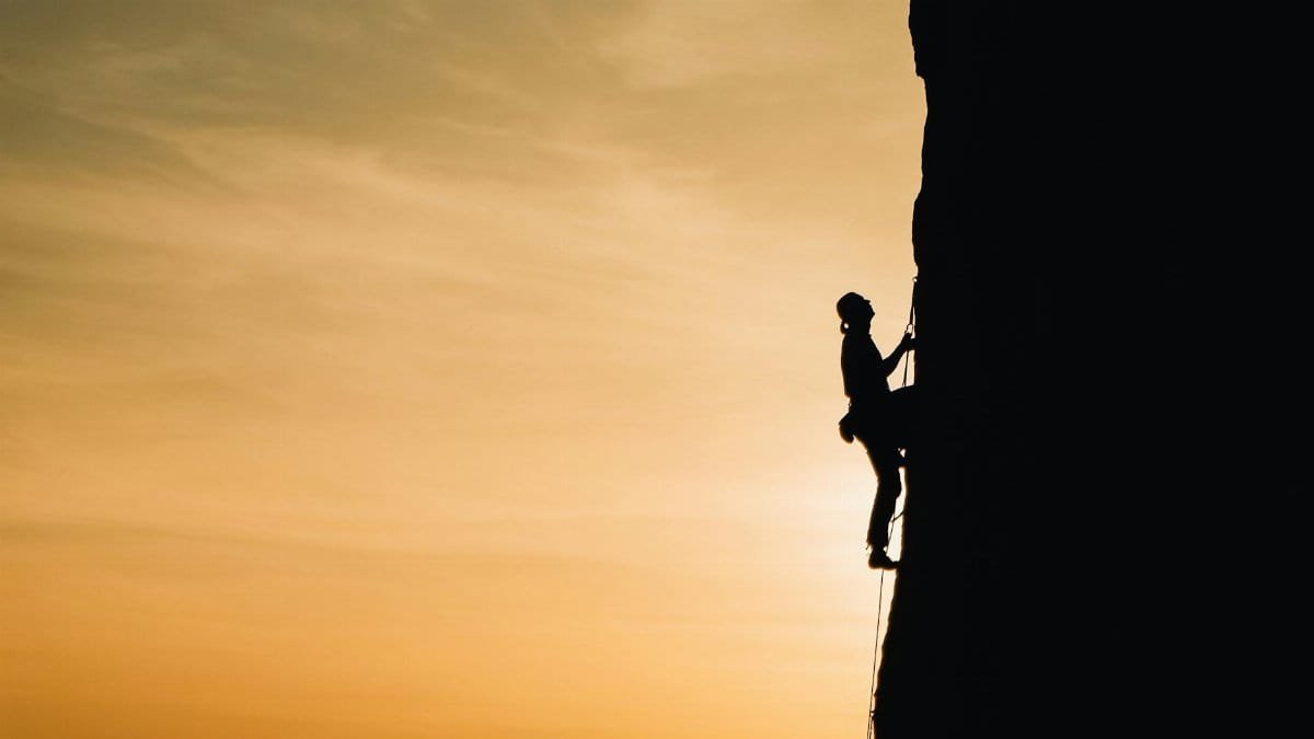 A silhouette of a rock climber scaling a steep cliff during sunset in Russia, showcasing determination and adventure.