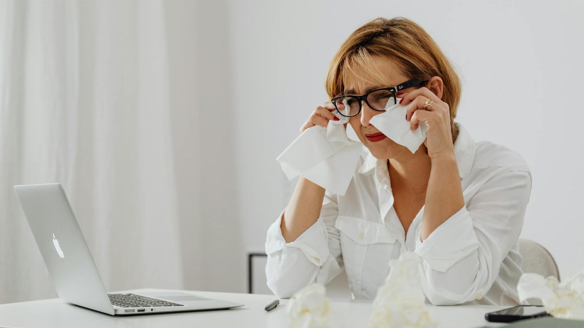 Woman experiencing stress at work using a laptop with tissues on a desk.