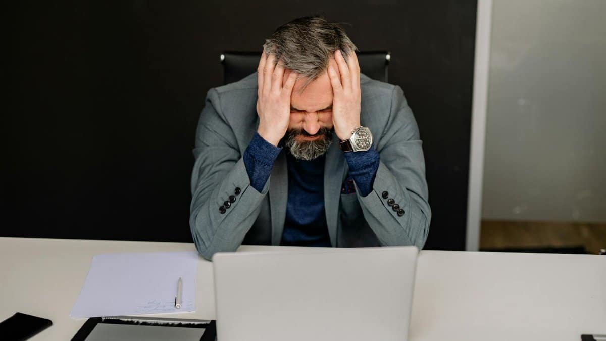 Businessman showing frustration with hands on head while working on a laptop in an office setting.