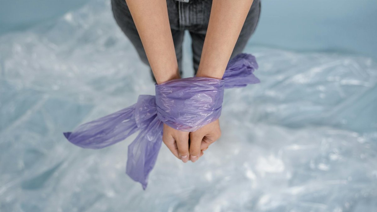 A pair of hands tied with a purple plastic bag, symbolizing constraint or captivity.