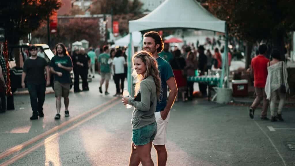 A couple enjoys a lively street festival in Fayetteville, Arkansas, surrounded by people and vibrant atmosphere.