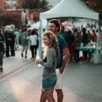 A couple enjoys a lively street festival in Fayetteville, Arkansas, surrounded by people and vibrant atmosphere.