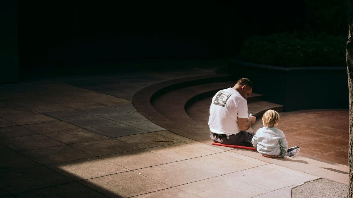 Father and son bonding outdoors, sitting on urban steps in the sunlight.