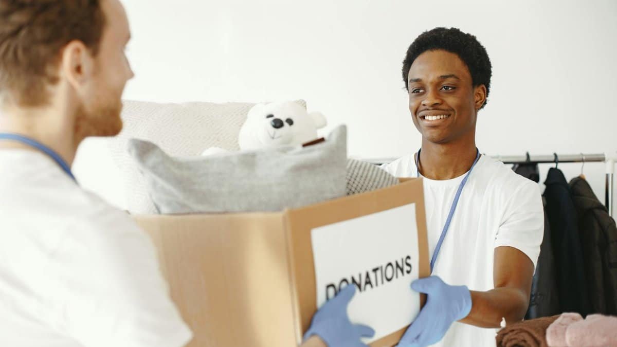 Two volunteers joyfully handing and receiving donation boxes full of clothes and toys.