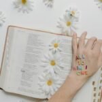 Open Bible adorned with daisies and letters spelling 'ALL TO HIM I OWE', emphasizing faith and inspiration.