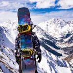 Snowboarder stands on snowy peak, gazing at breathtaking mountains in Breckenridge, Colorado.