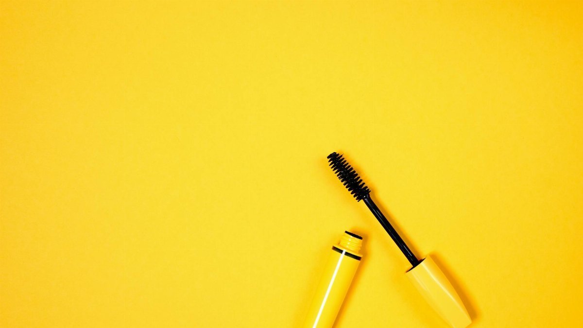 Open mascara with brush on vibrant yellow background, perfect for beauty and cosmetic themes.