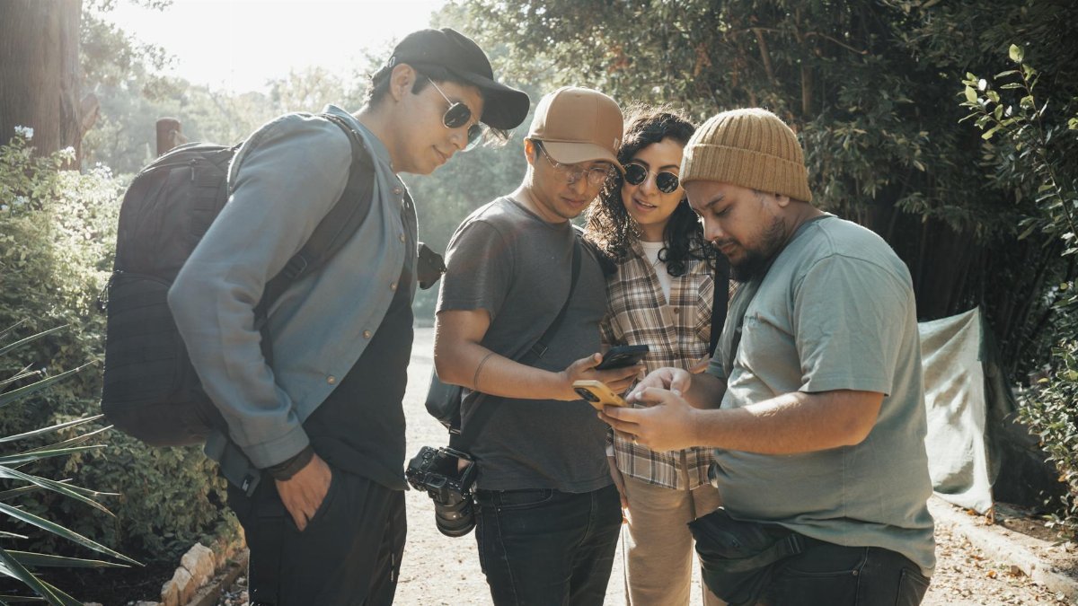 A diverse group of friends explores outdoors while engaging with their smartphones, enjoying leisure time.