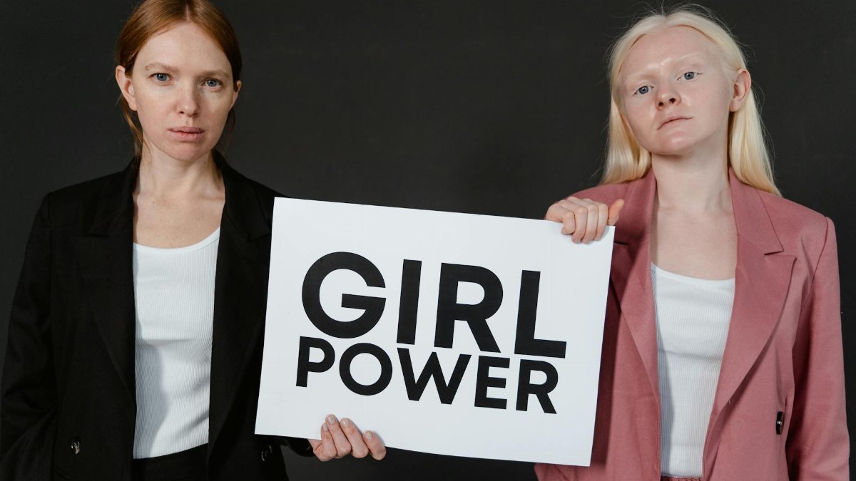 Two women stand confidently holding a 'Girl Power' sign, symbolizing empowerment and equality.