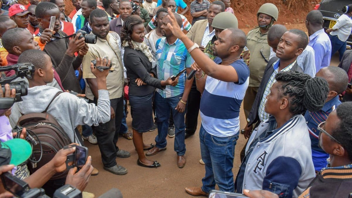 A diverse group discusses community issues with a politician in an outdoor setting.