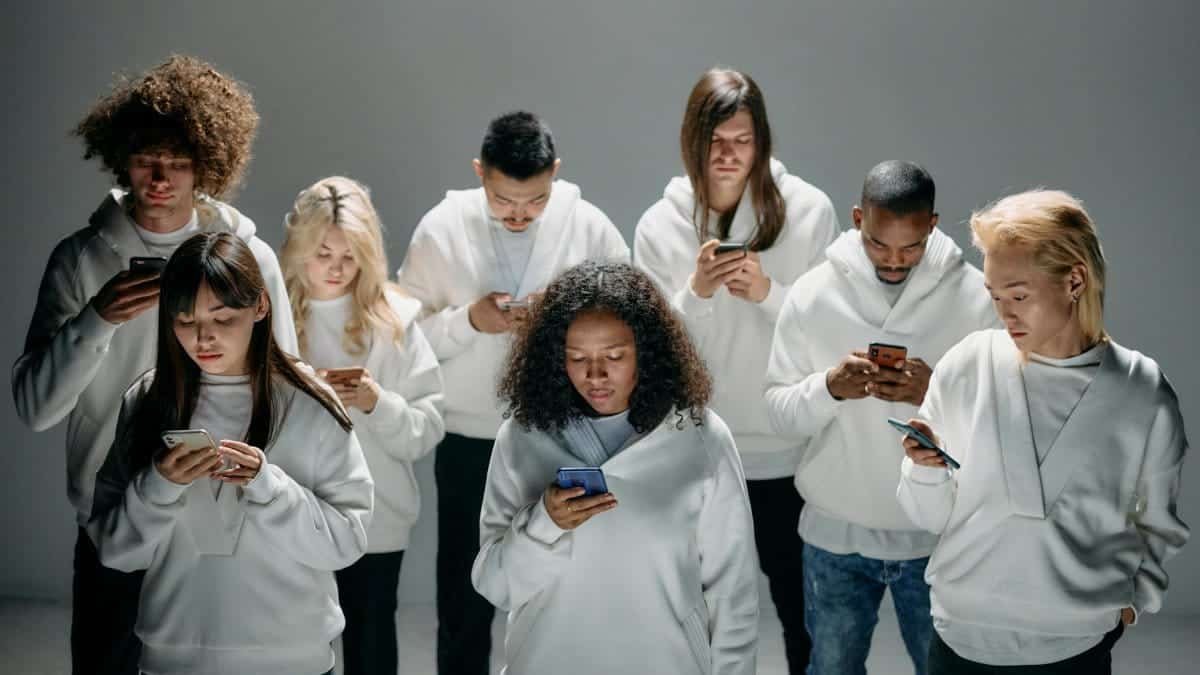 A diverse group of people in white hoodies engaged with smartphones, symbolizing social connection and isolation.